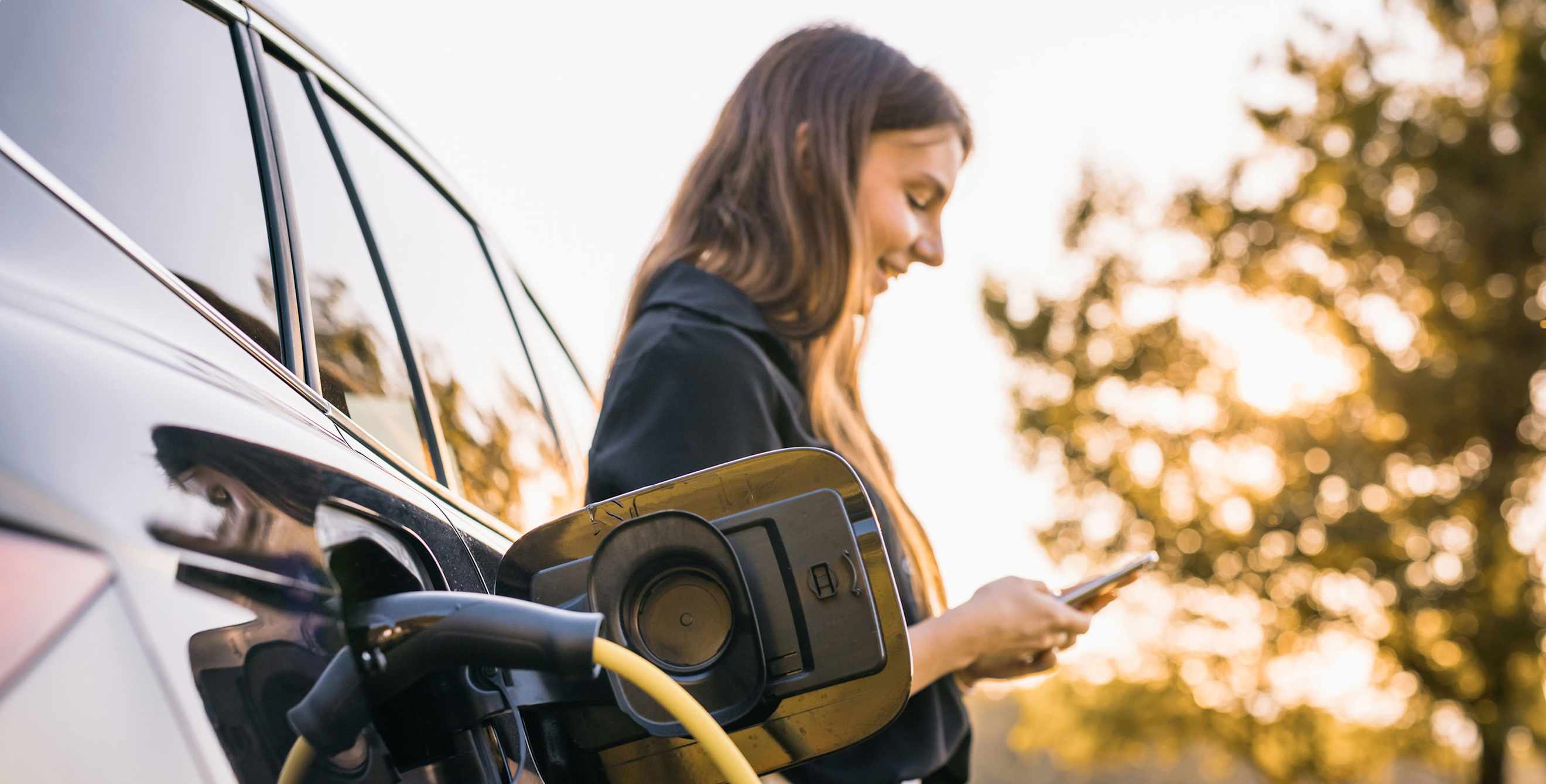 A woman charges her EV on a fall day.
