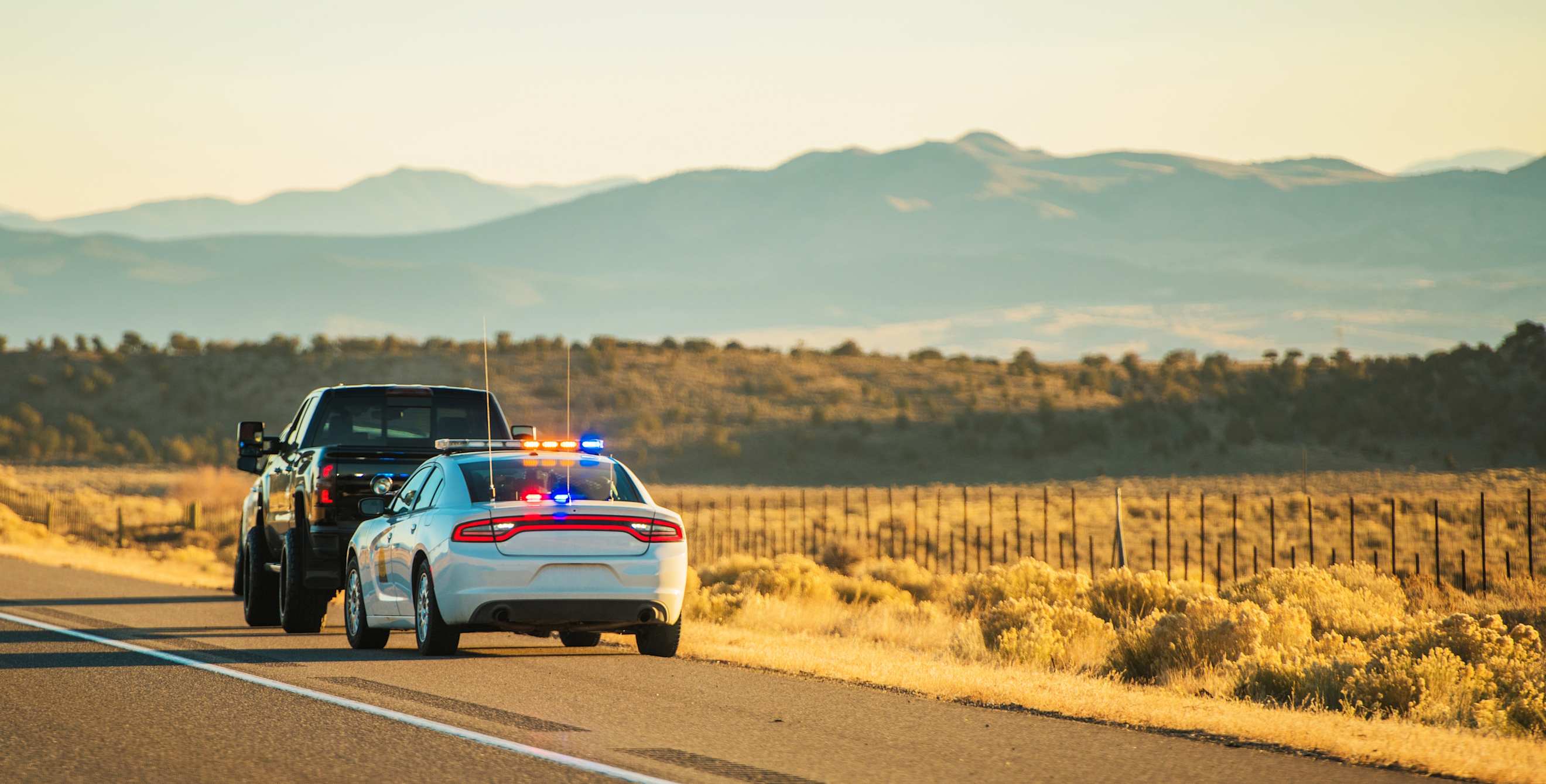 A Utah Highway Patrol car with flashing lights is pulled over behind a black truck on the side of a highway.