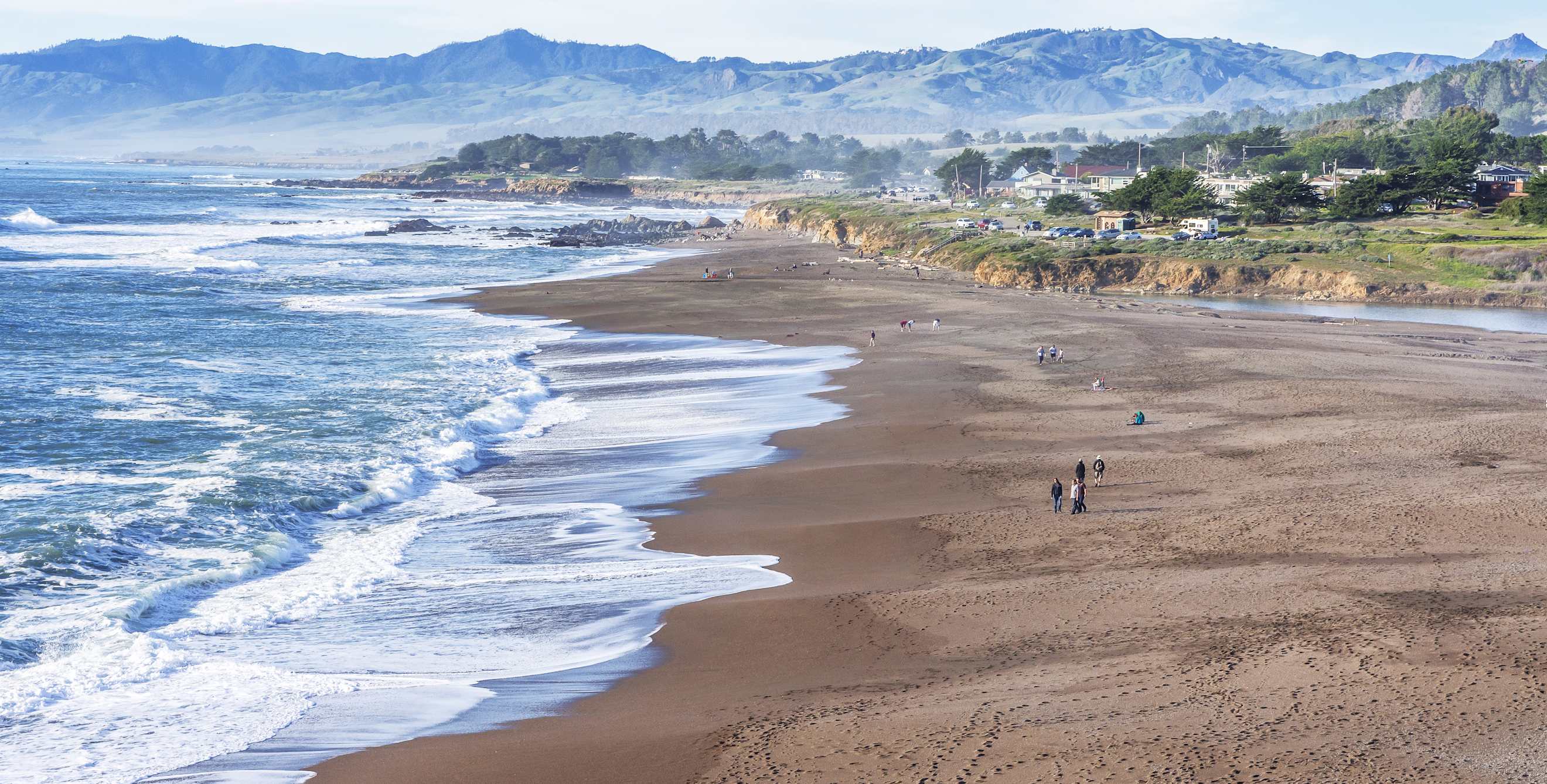 People walk along the sand at Moonstone Beach in Cambria, California.