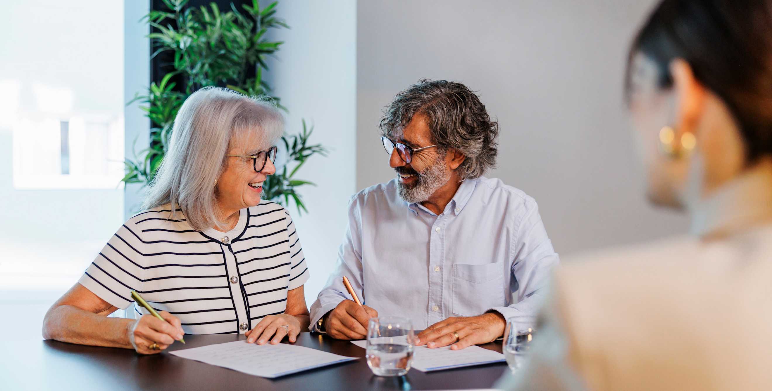 An older couple sign their estate trust and will paperwork with their lawyer.