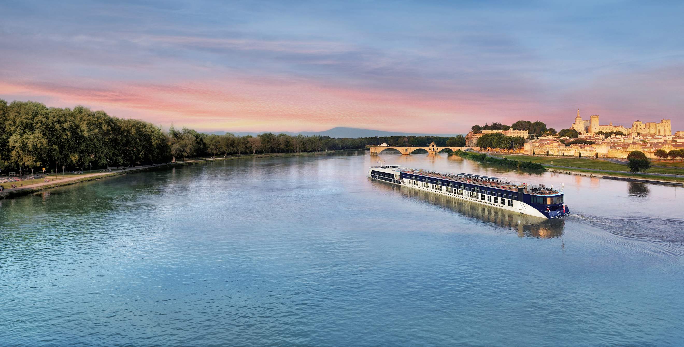 A river boat cruises past Avignon, France at sunrise.