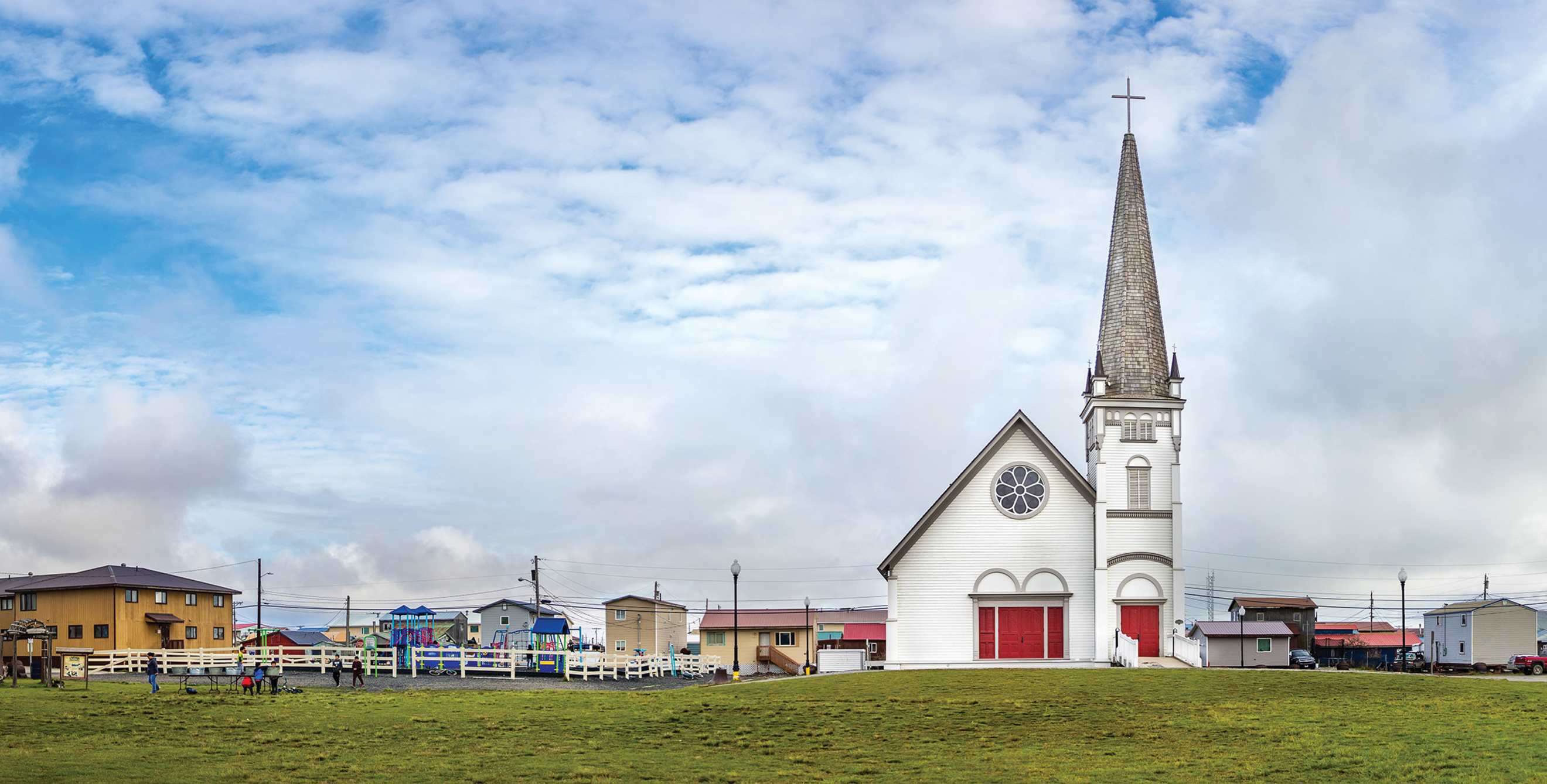 a panoramic photo of a city square in Alaska with green grass and a blue sky