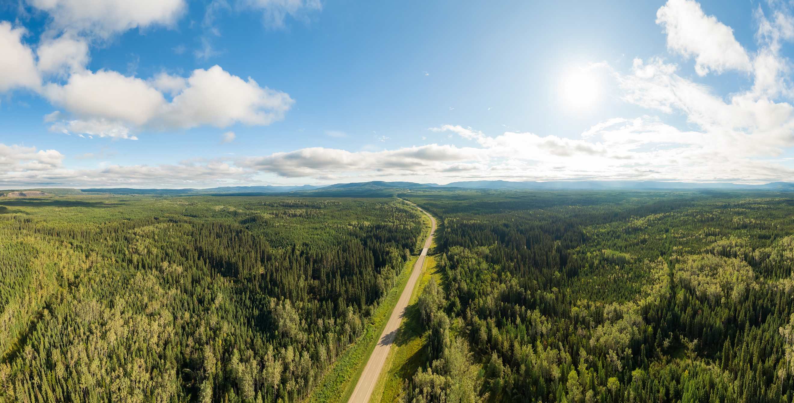a panoramic view of a highway cutting through green forest with blue skies above