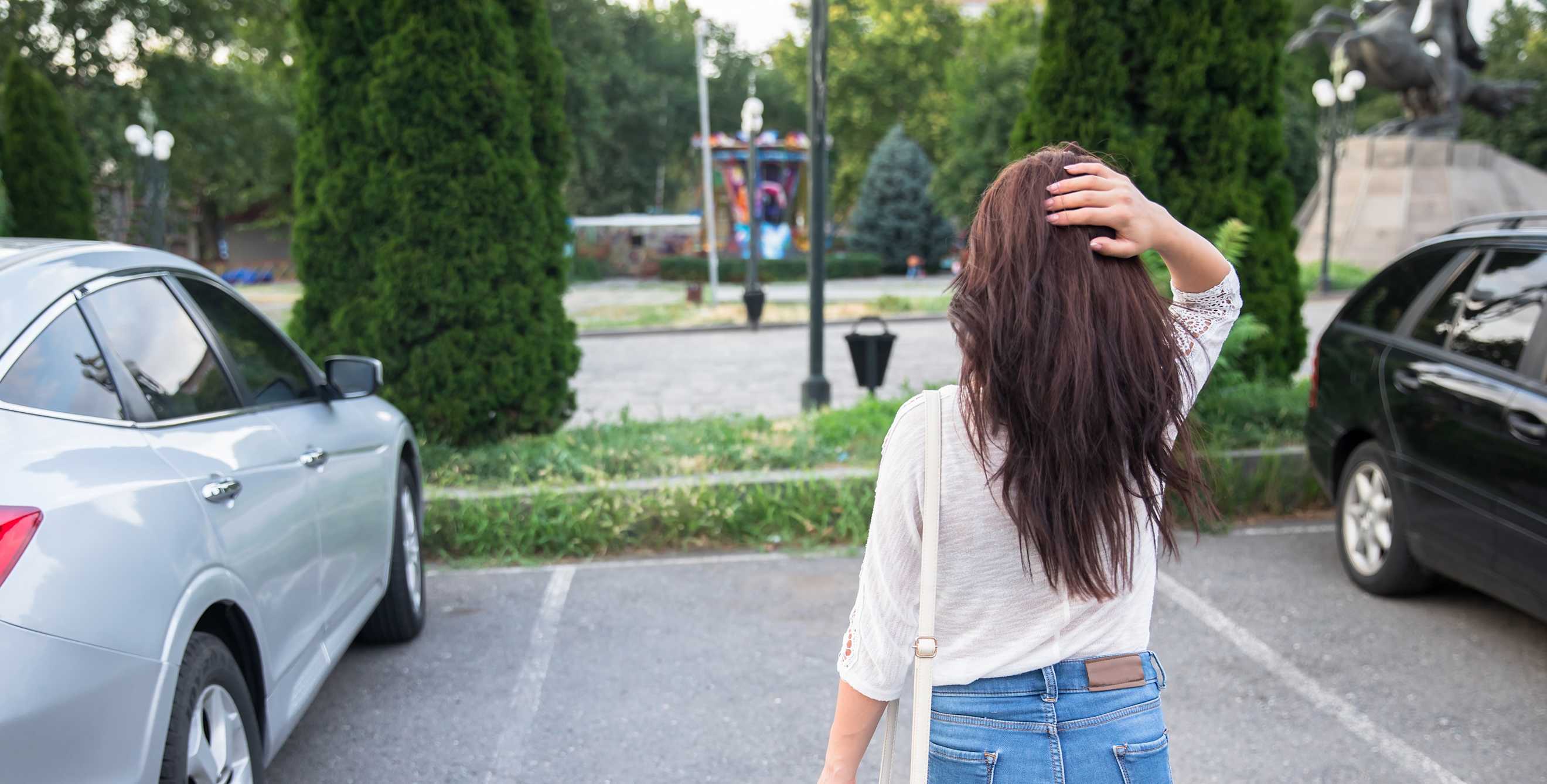 a woman with brown hair stands in front of an empty parking space with her head on the back of her head looking upset that a car is not there