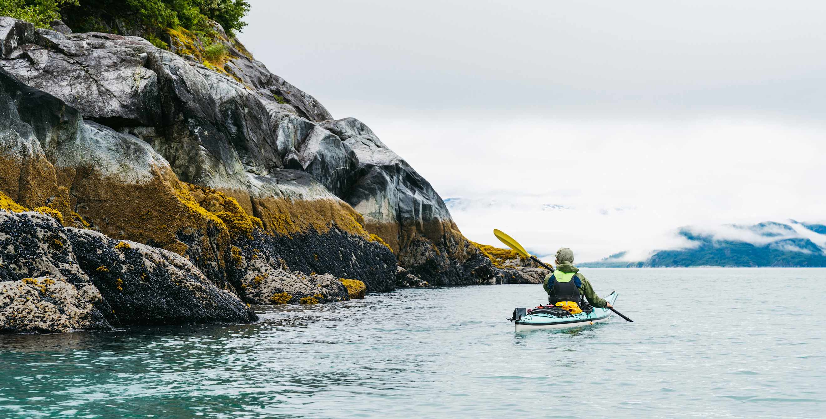 a person kayaks next to a pristine mountain in Alaska