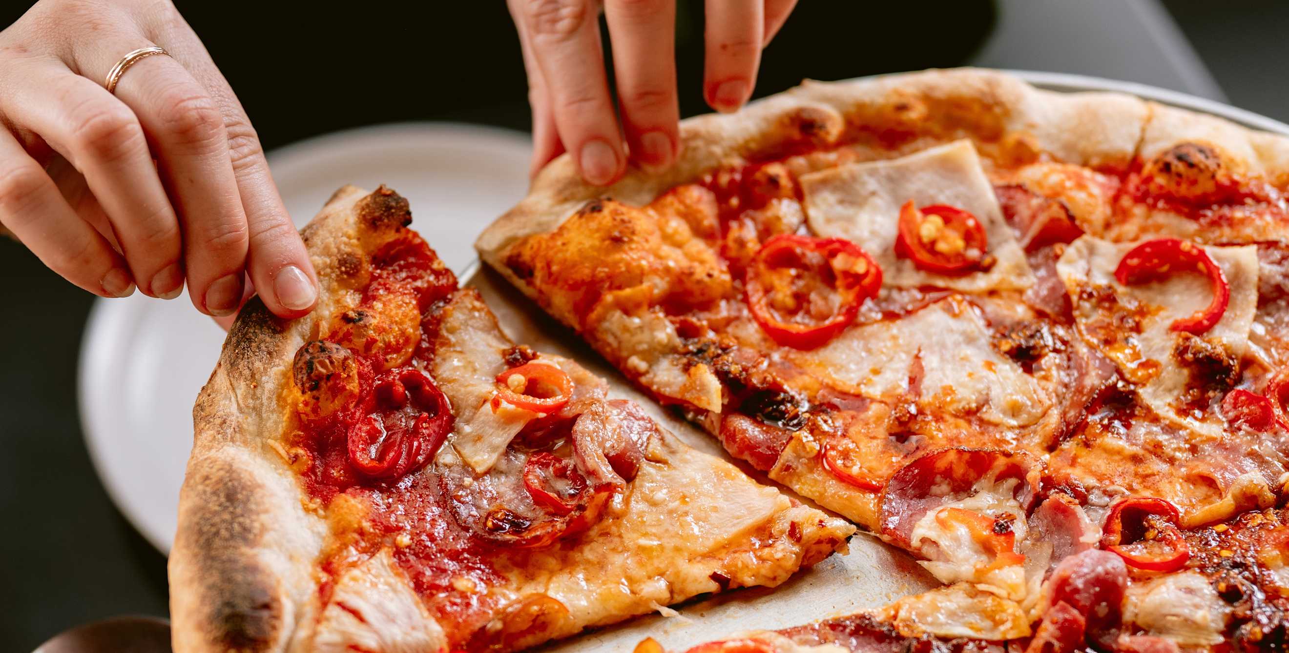 a person serves a slice of pizza with red peppers on it