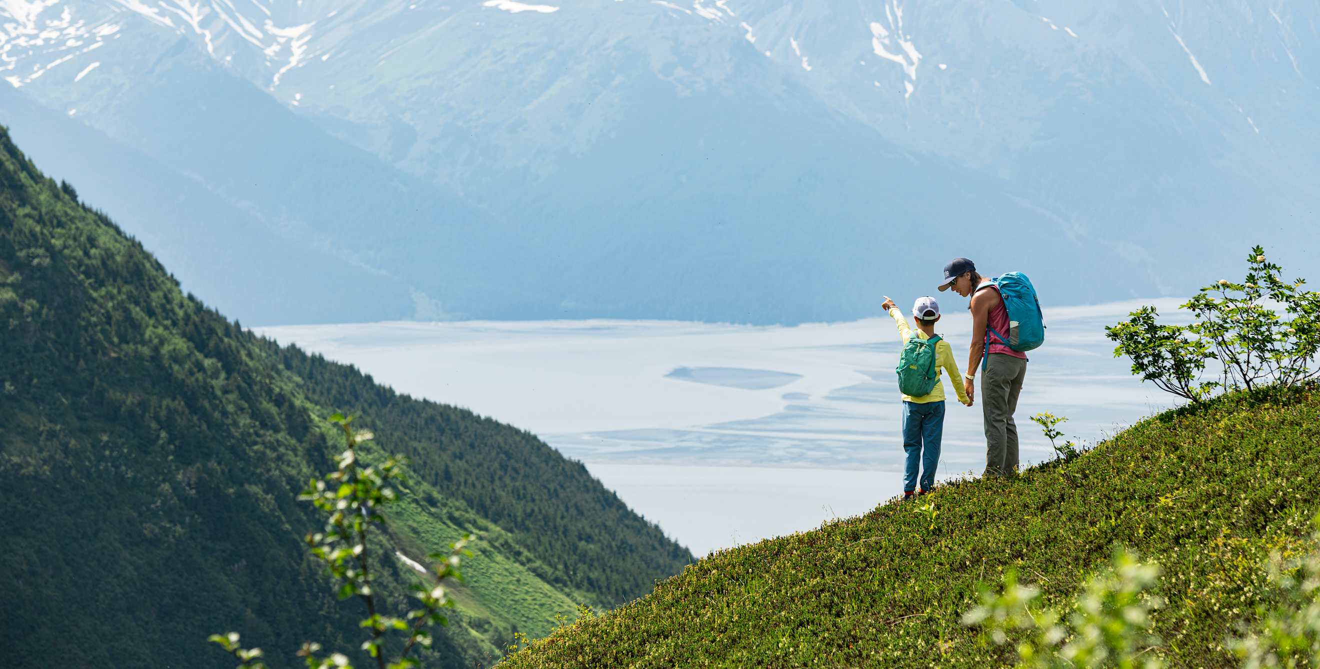 a mom and young son stand on a hike pointing out at an epic mountain view in Alaska