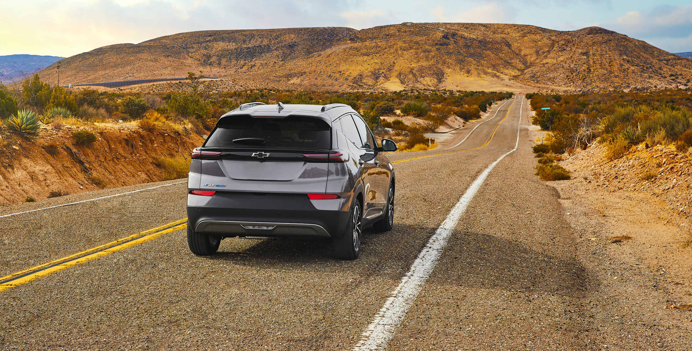 An EV Chevy Bolt SUV drives along a desert highway.