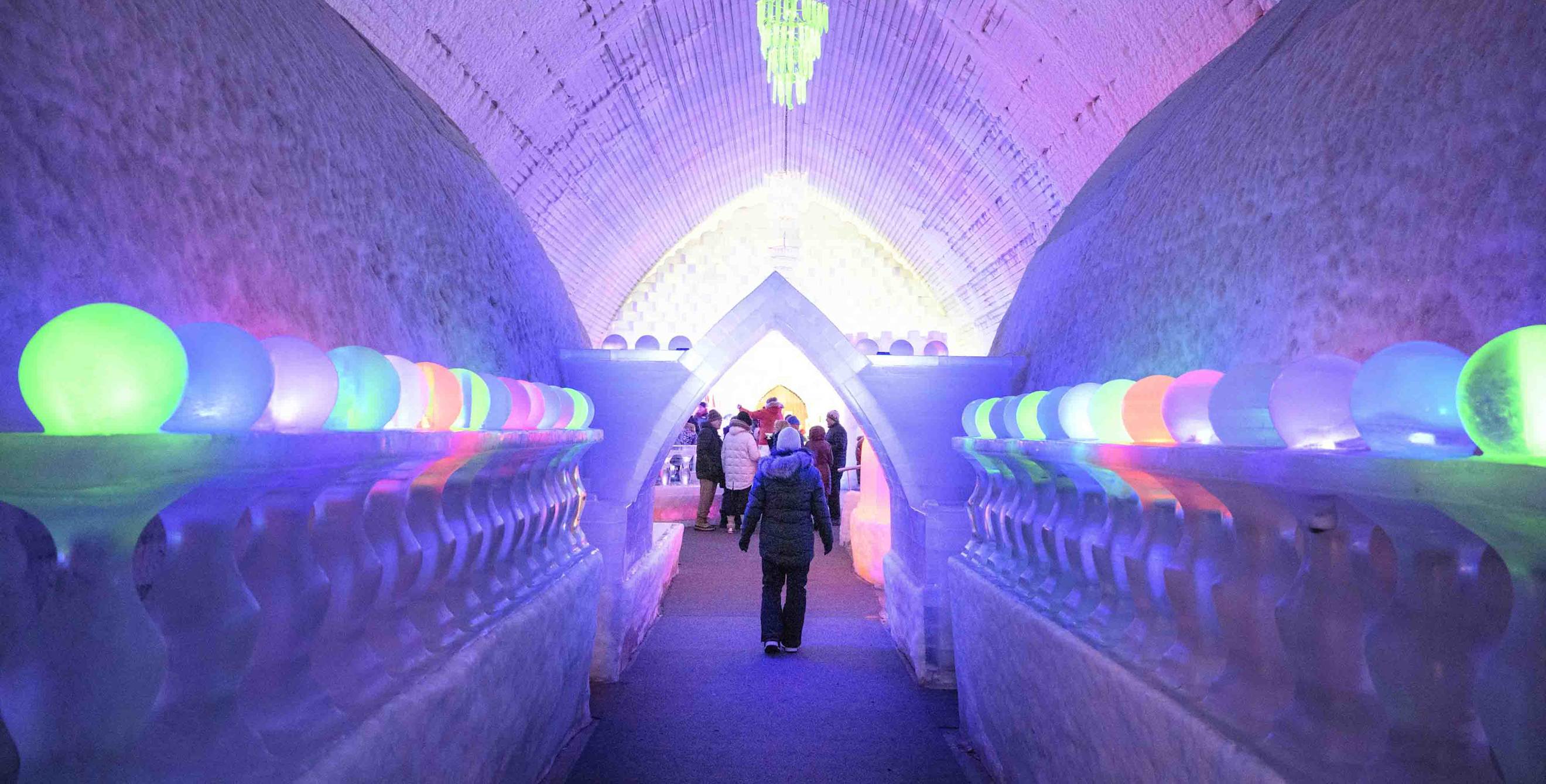 a person walks through a colorfully lit ice cave