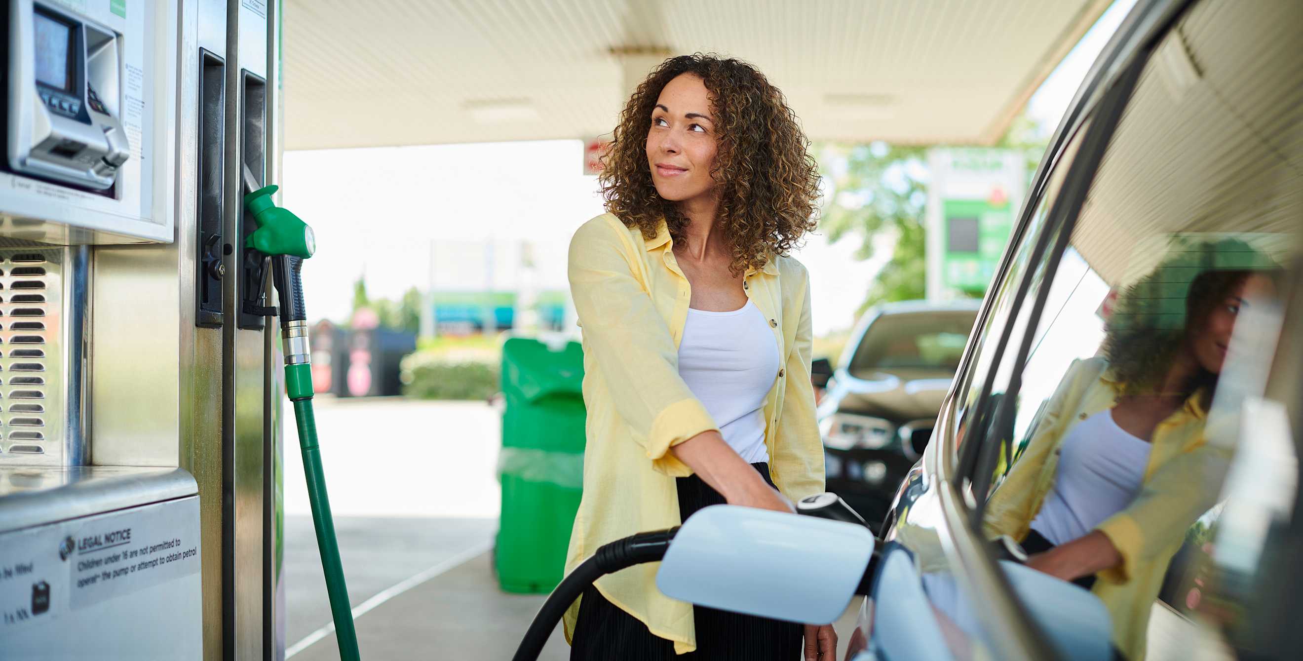 A woman fills her car at a gas station.