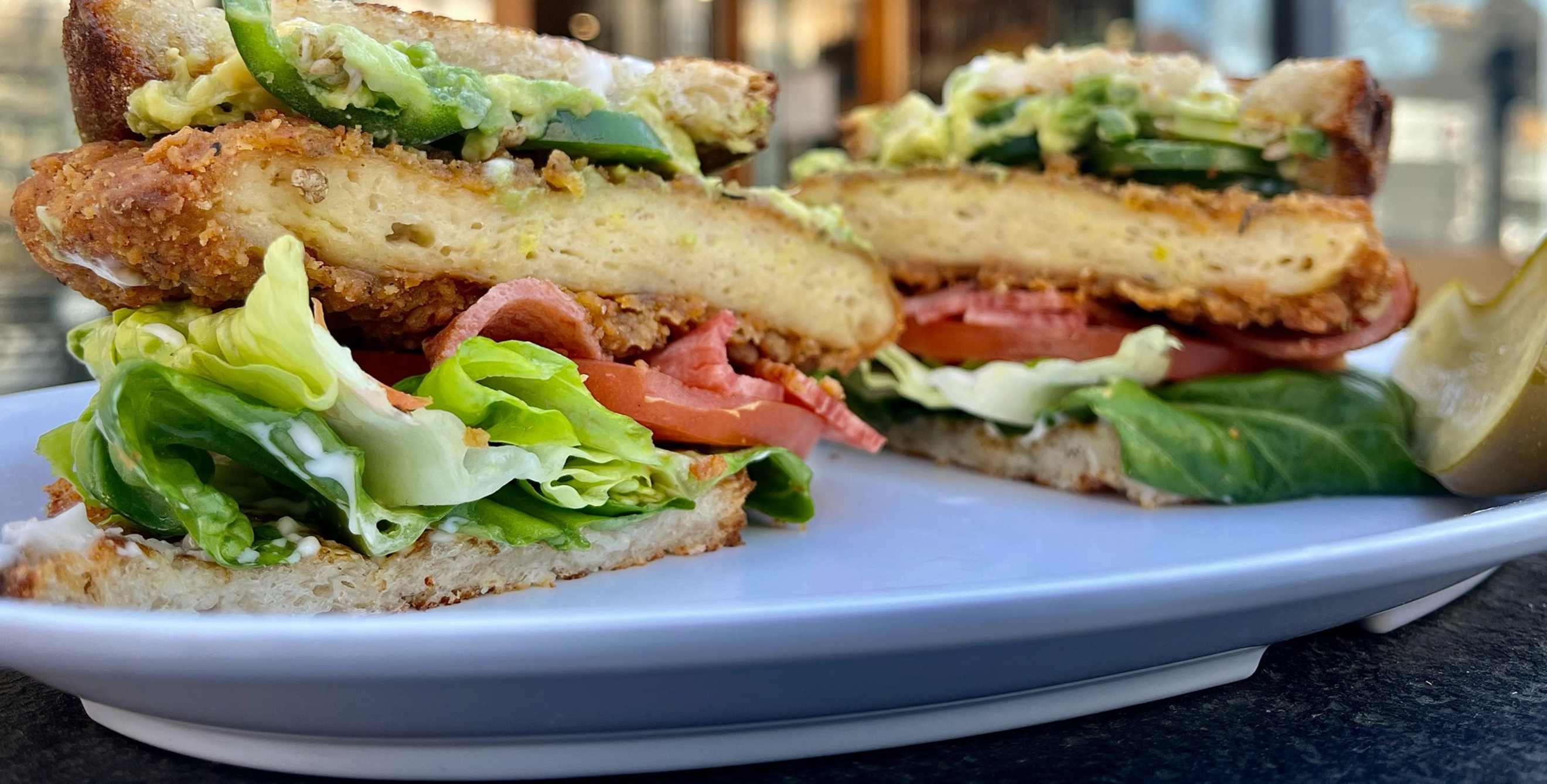 a vegetarian sandwich on a plate outside a restaurant called the butcher's son