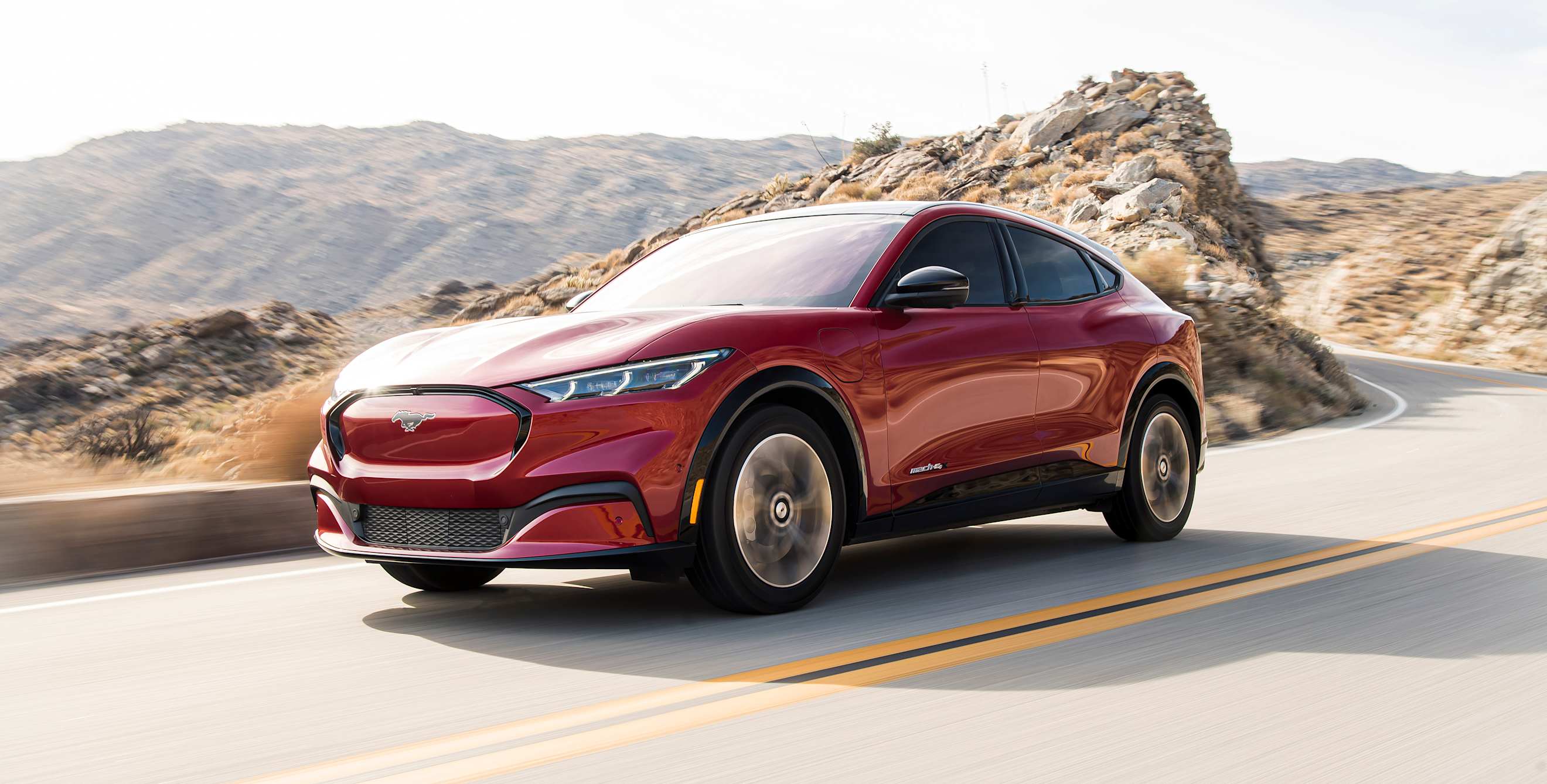 A red 2021 Ford Mustang Mach-E on a desert highway.