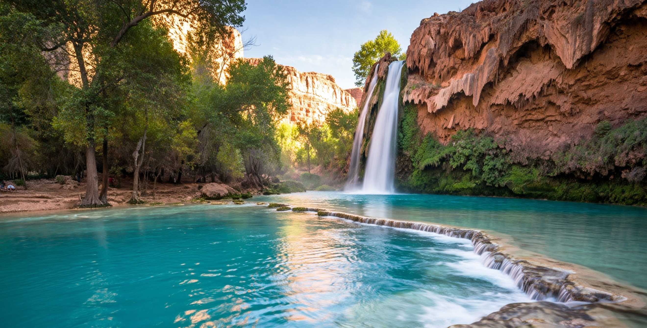 Turquoise water beneath Havasu Falls in Arizona surrounded by red rock and greenery.