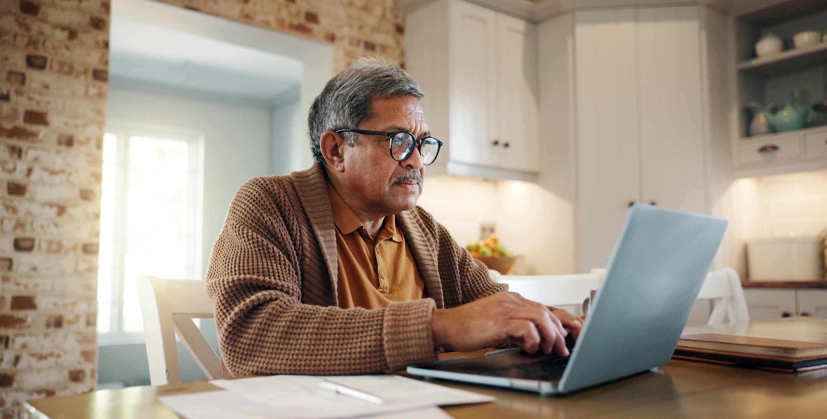 An older man uses his computer at the dining room table.