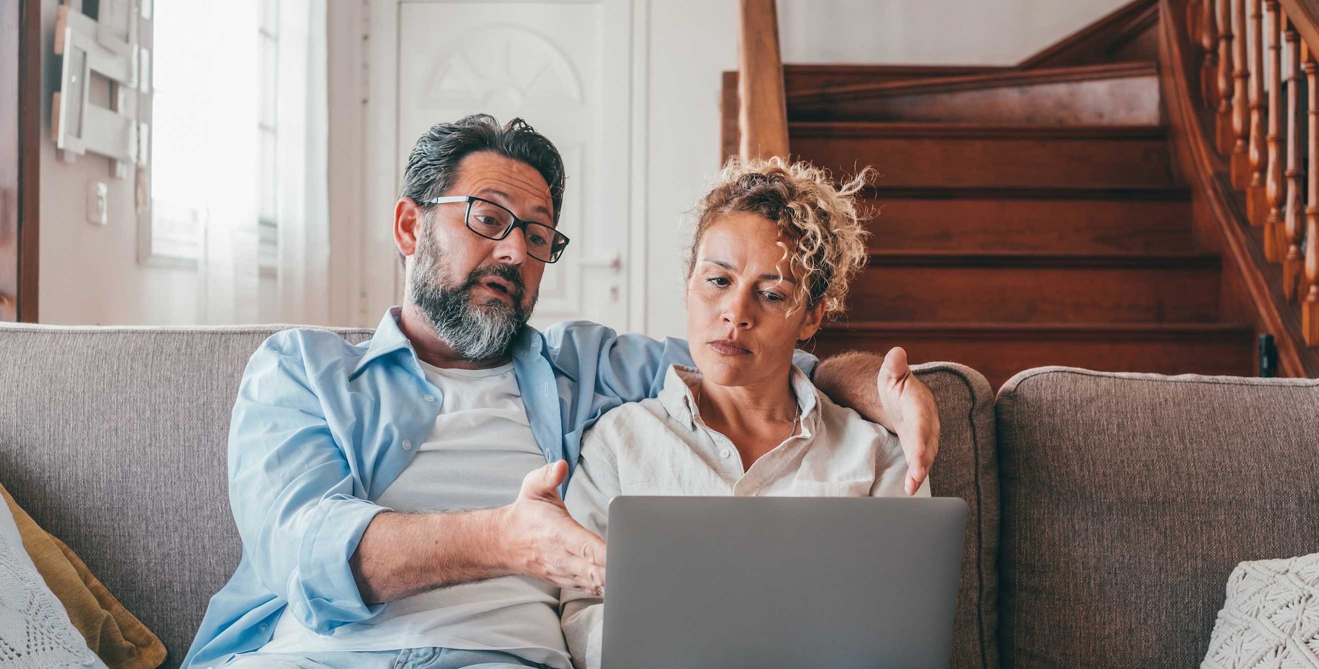 A couple look at a computer together while sitting on the couch.