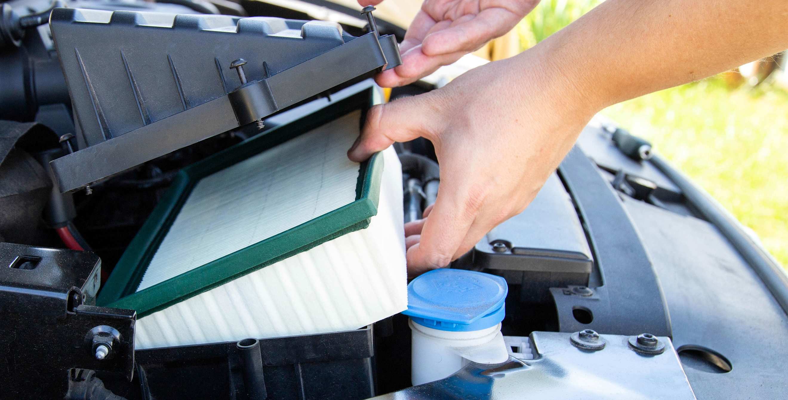 A person replaces their car engine air filter.