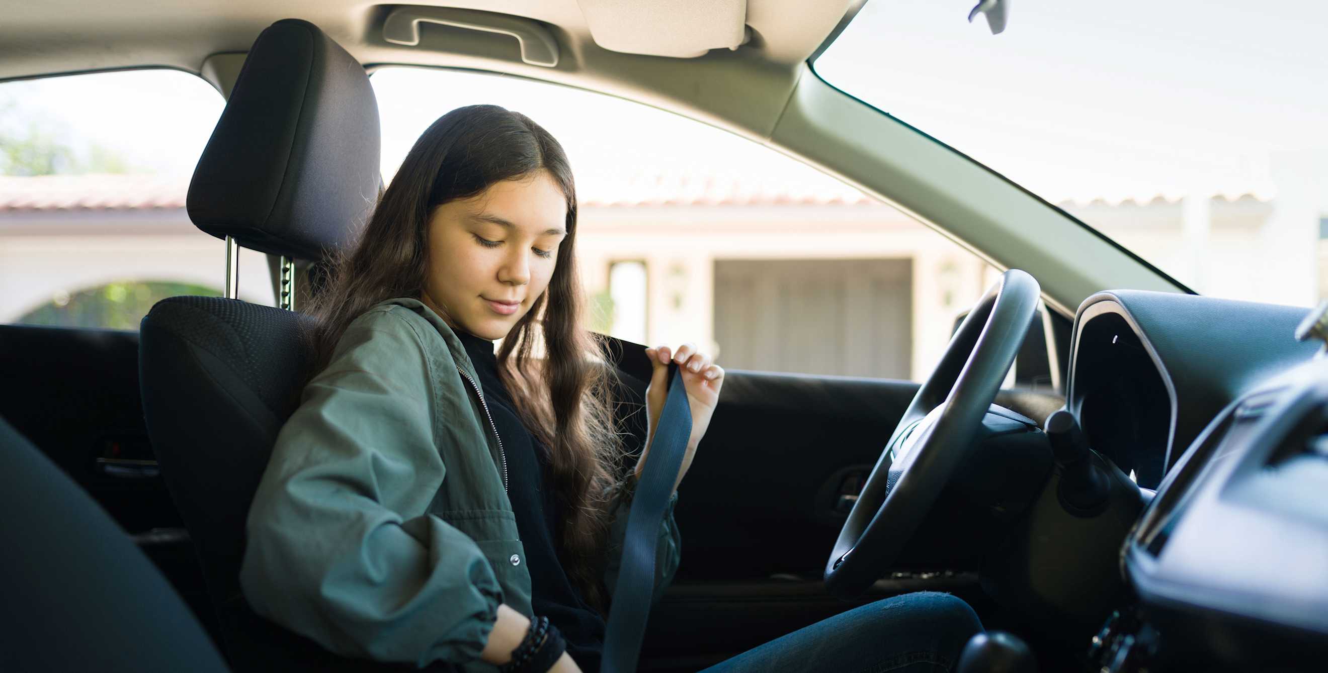 A teen puts on her seatbelt before driving on a sunny day.