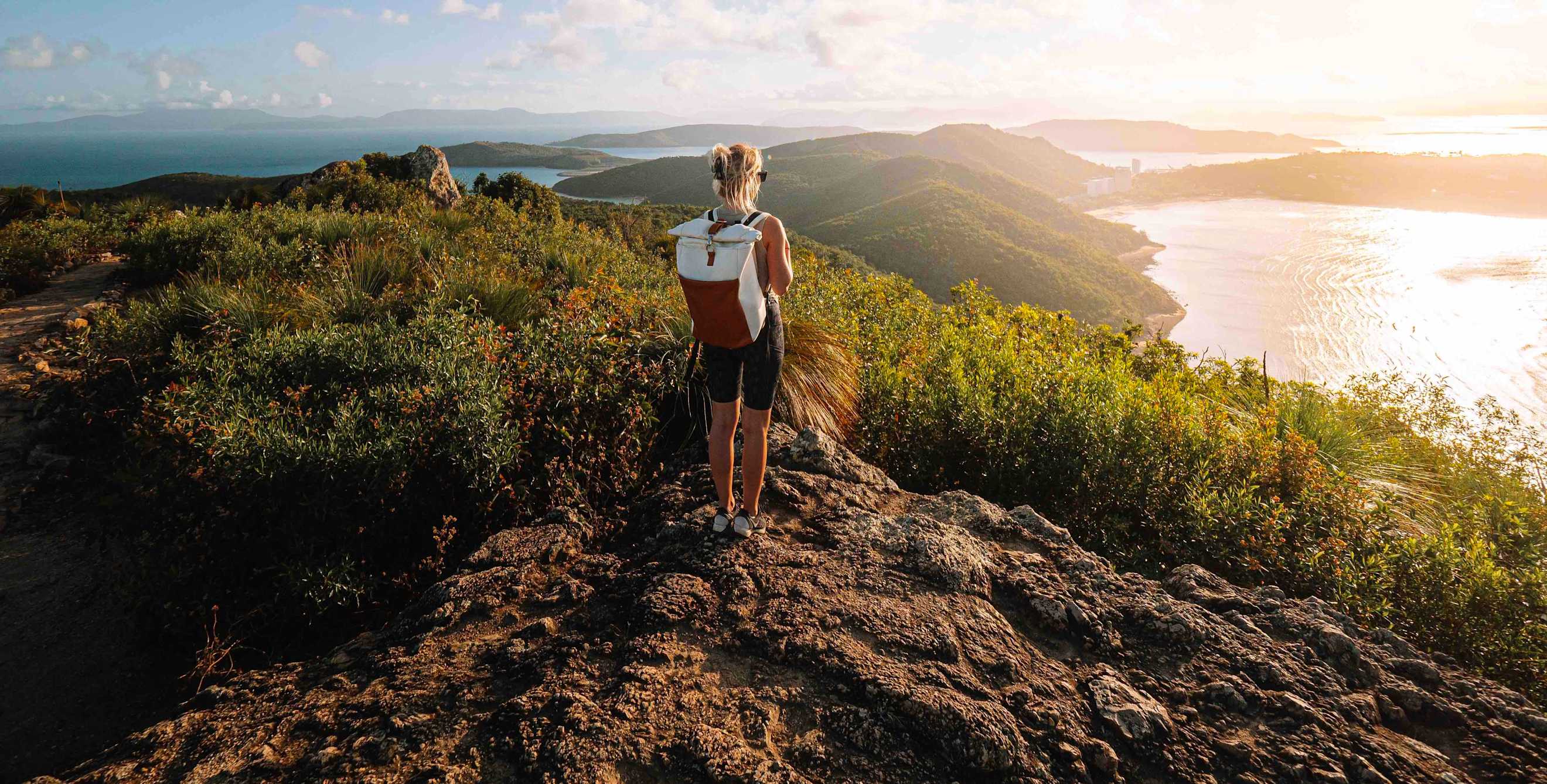 a woman stands on top of a mountain looking out at the ocean in the sun