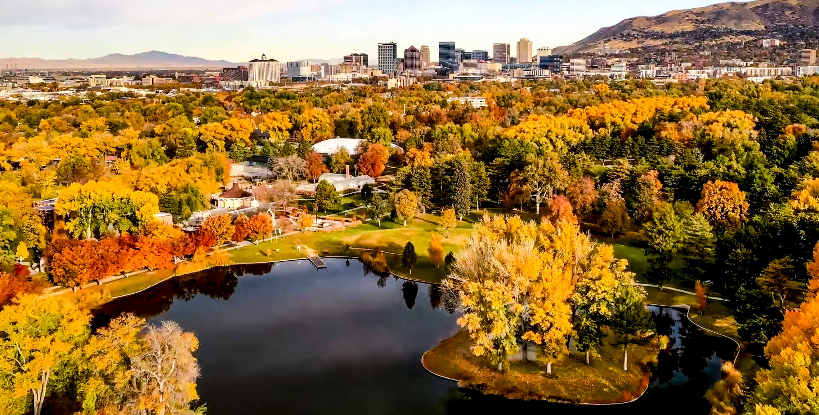 Liberty Lake surrounded by trees in fall colors under blue, partly cloudy sky at Liberty Park in Salt Lake City, Utah