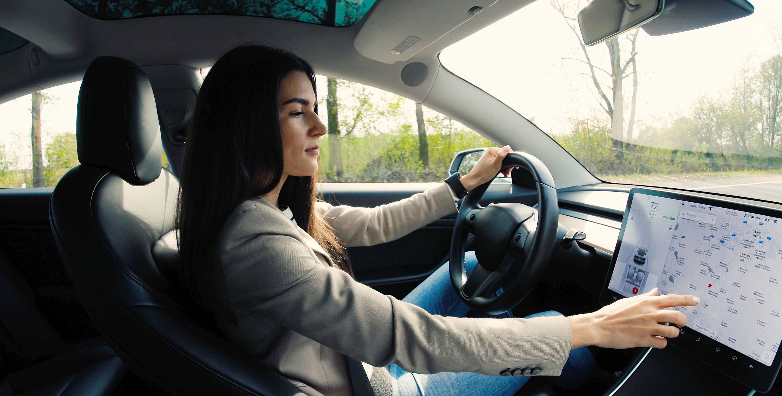A woman uses a large dashboard infotainment touch screen while driving.