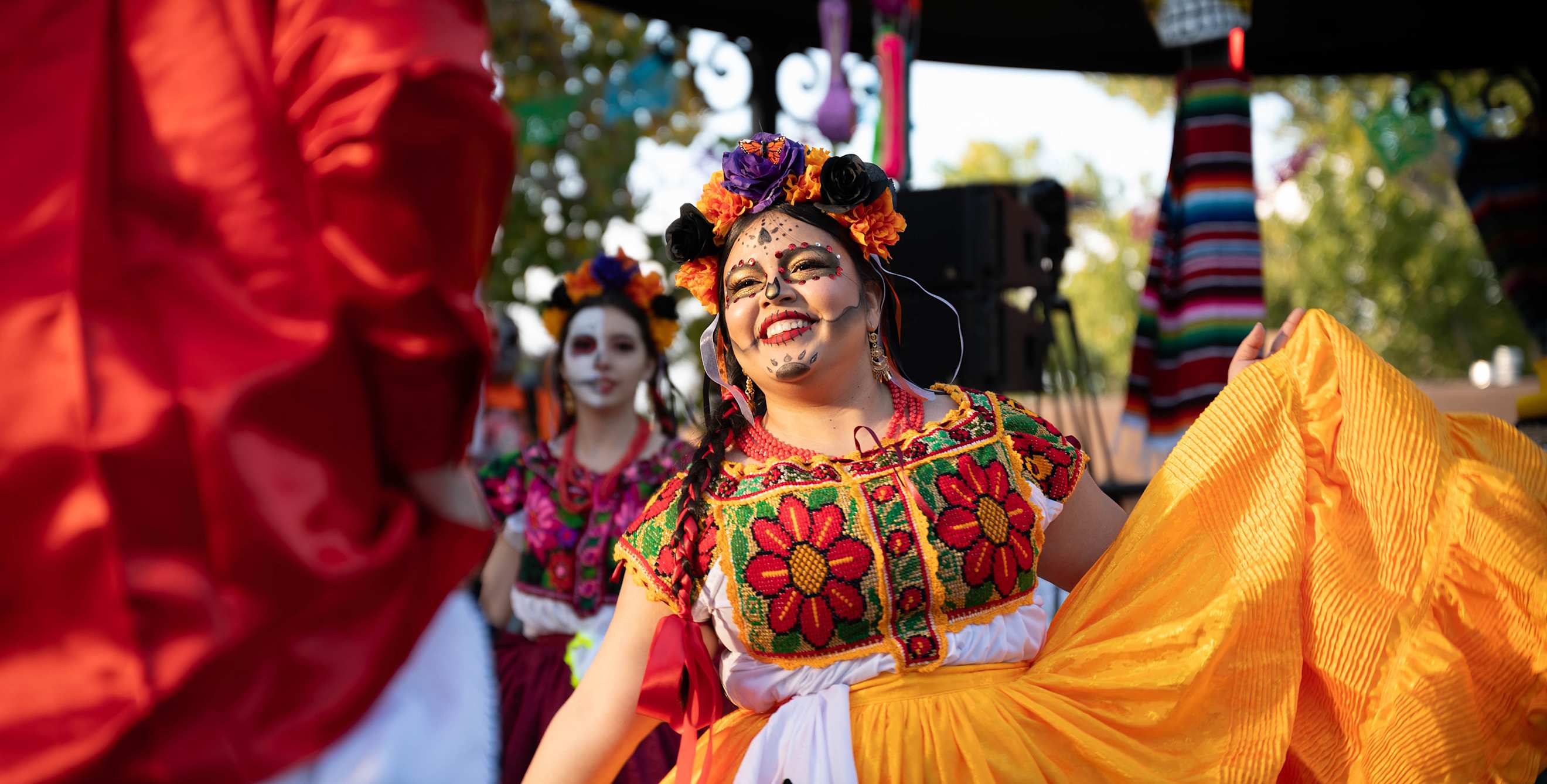 a woman in a colorful dress and face paint dances at a day of the dead celebration