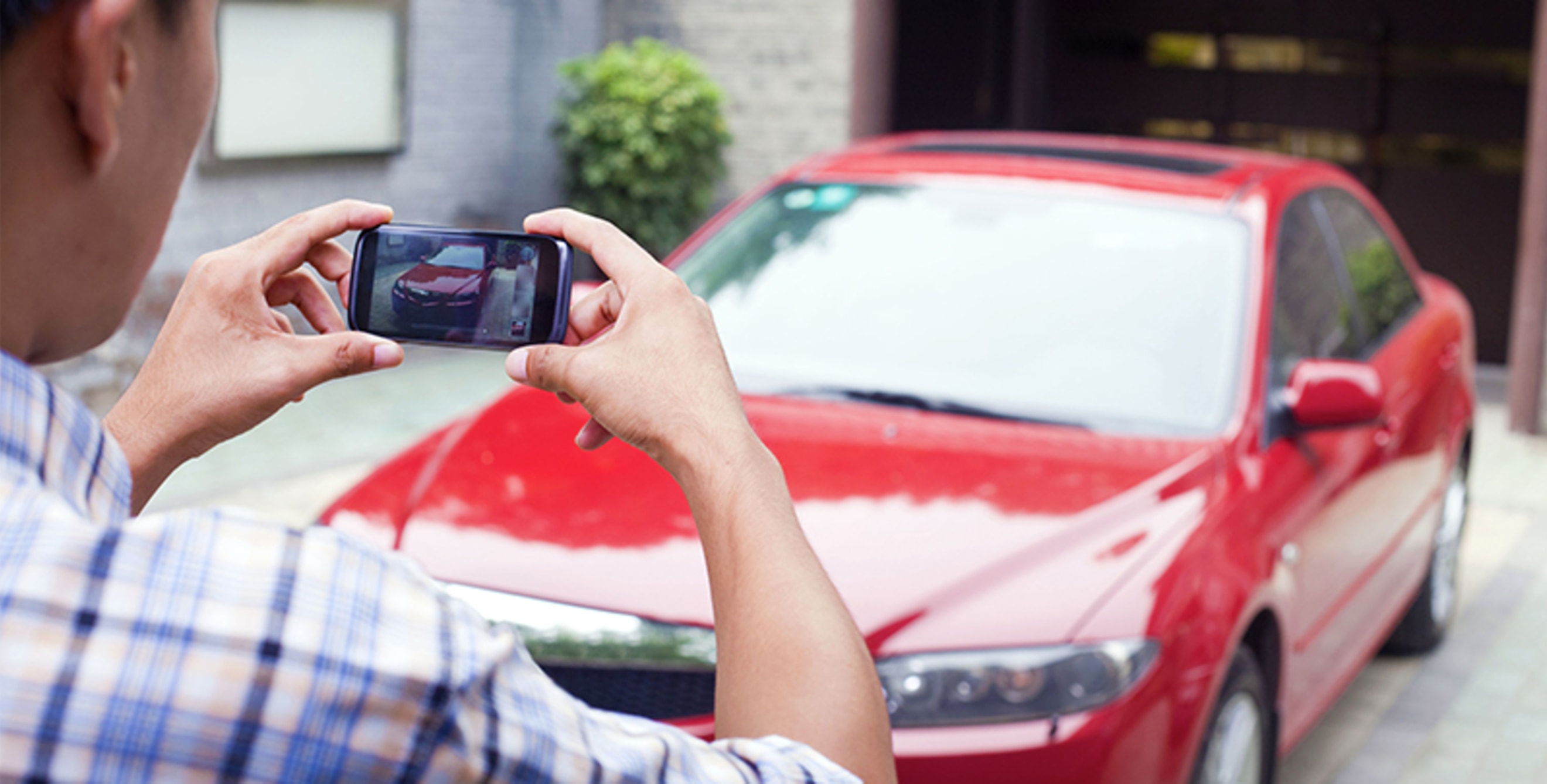 A man takes a picture of his red sedan to sell it.