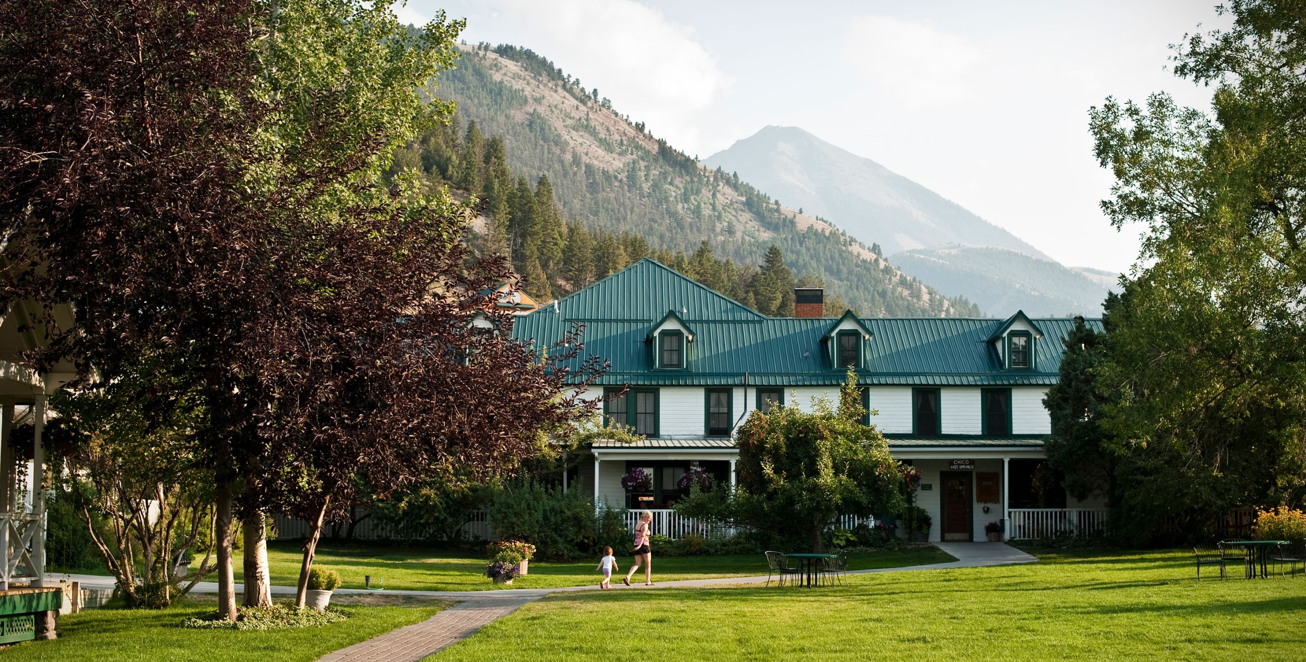 A mother and child walk outside at Chico Hot Springs in Pray, Montana with the mountains in the background.