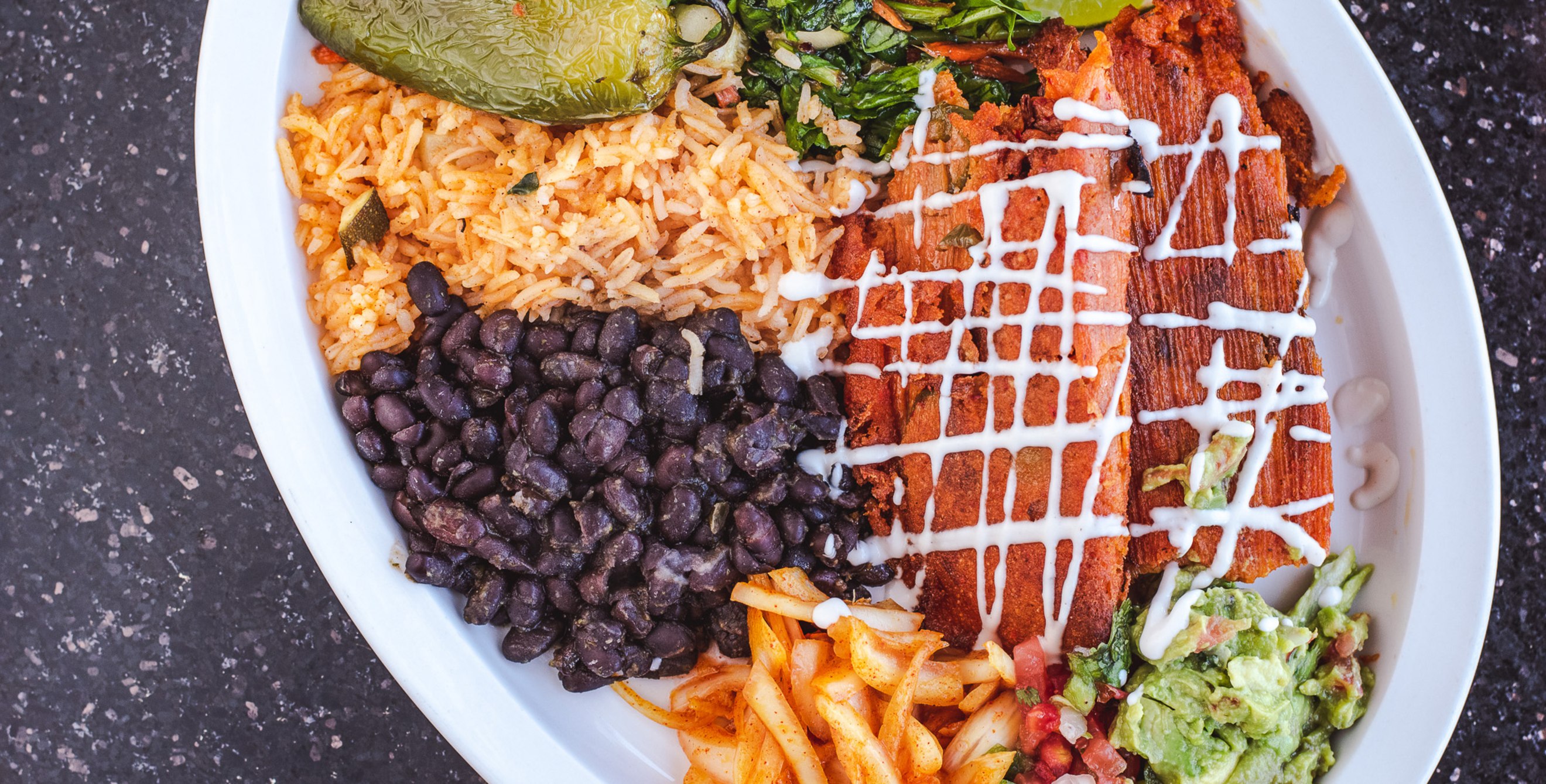 Tamales drizzled with sour cream served with black beans, rice, salsa and guacamole on a plate from Tumerico in Tucson, Arizona.