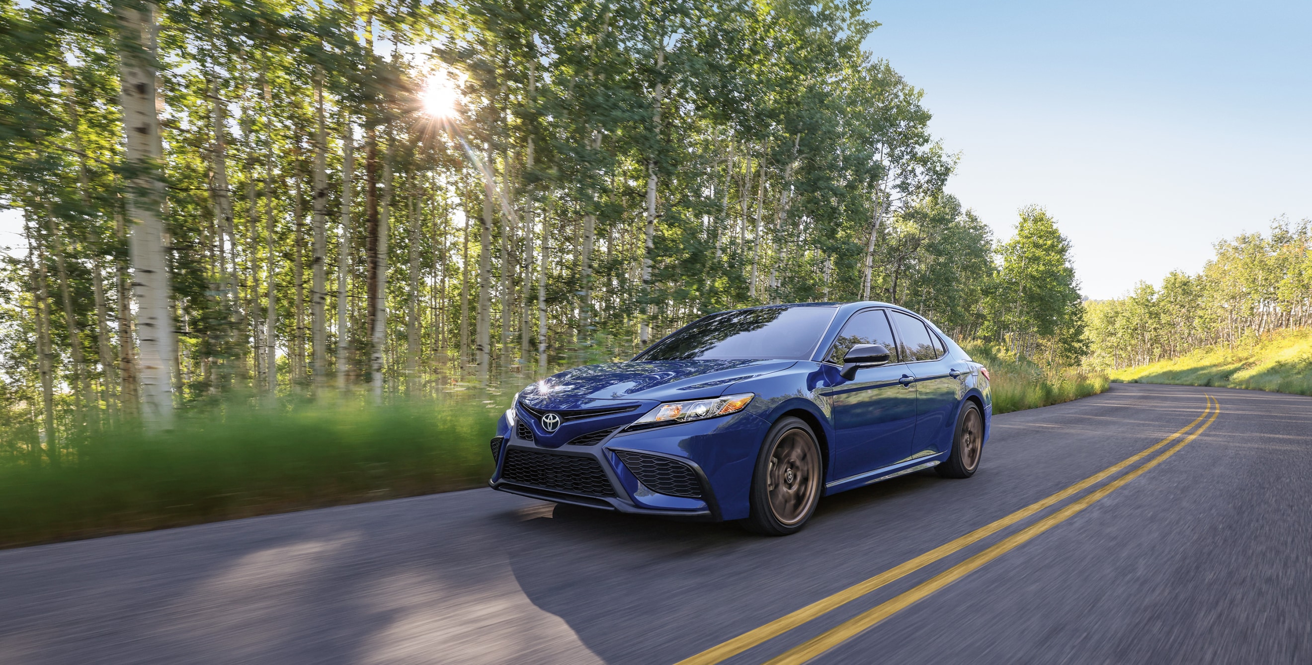 2023 Toyota Camry Hybrid SE Nightshade on a tree-lined road.