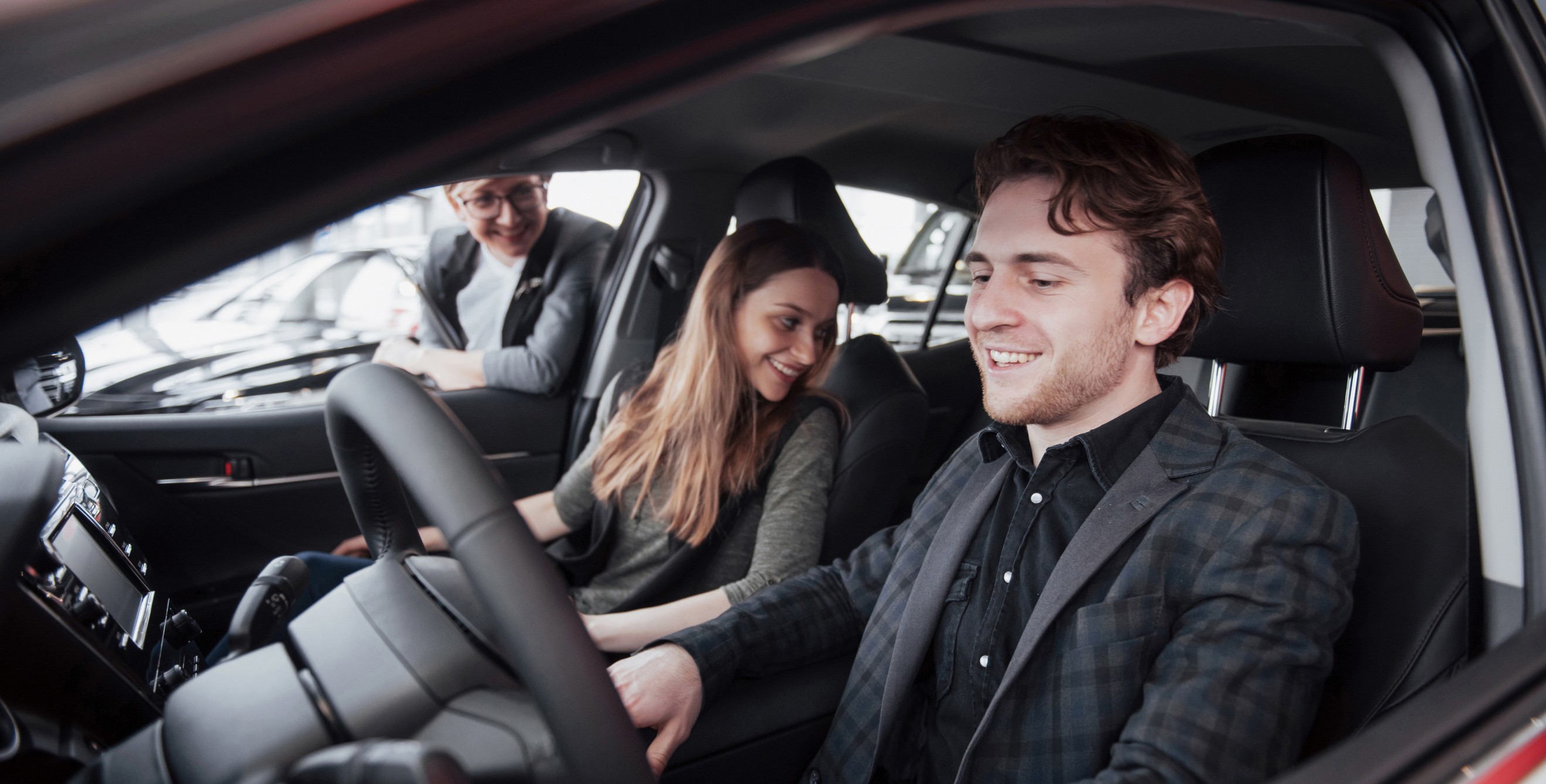 A couple sit in a new car in a dealership.