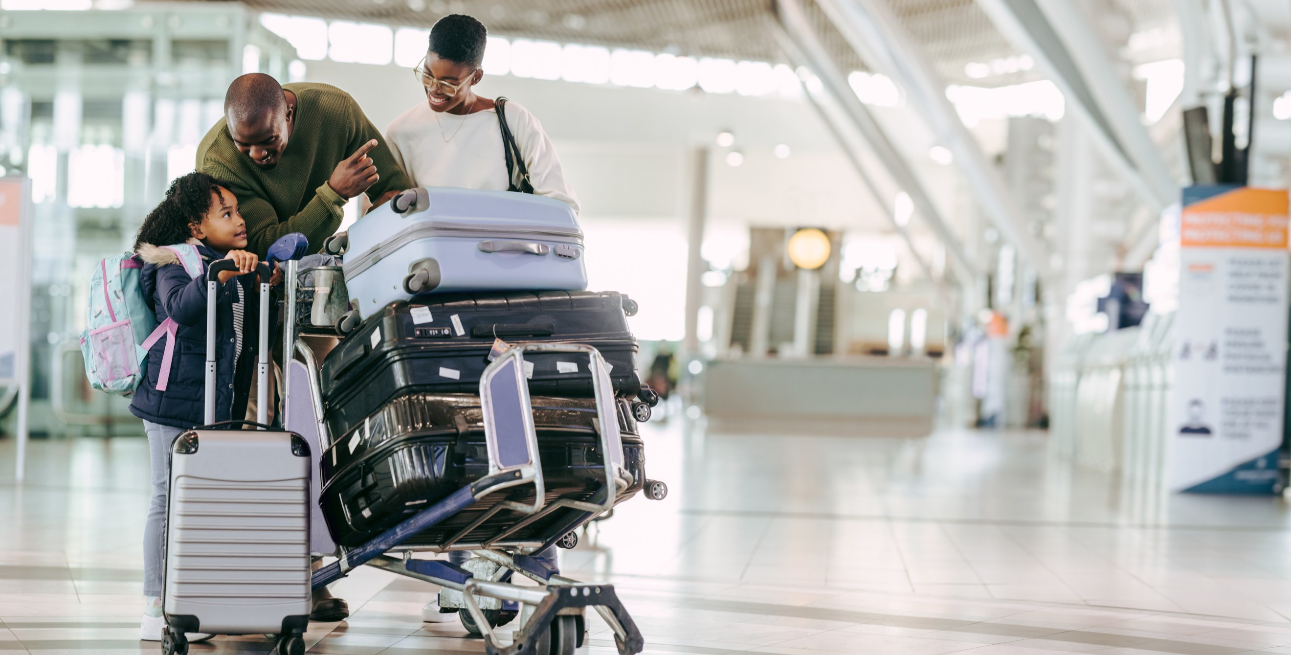 Family members navigate the airport together with a luggage cart.