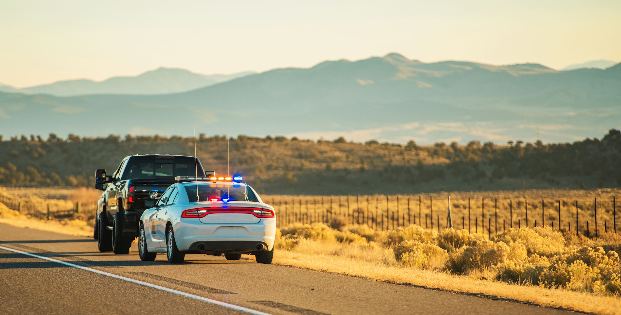 A Utah Highway Patrol car with flashing lights is pulled over behind a black truck on the side of a highway.
