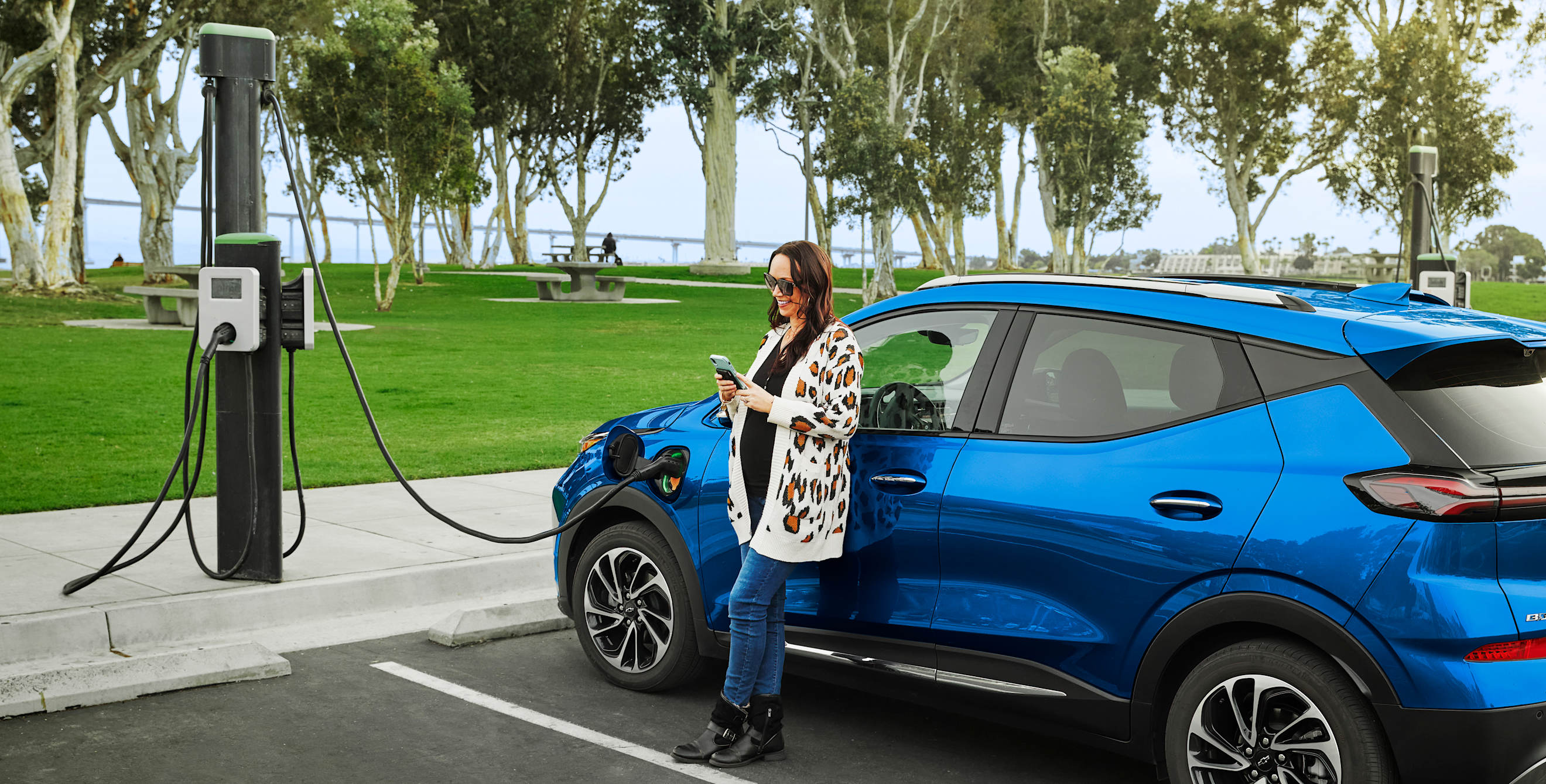 A woman charges her blue Chevrolet Bolt EV at a public charging station.