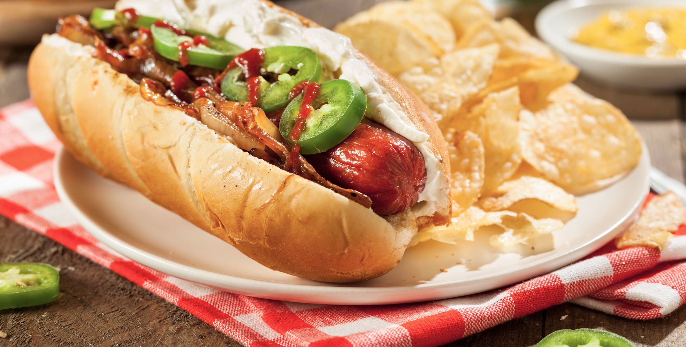 Seattle style hot dog with cream cheese and onions on a plate with potato chips.