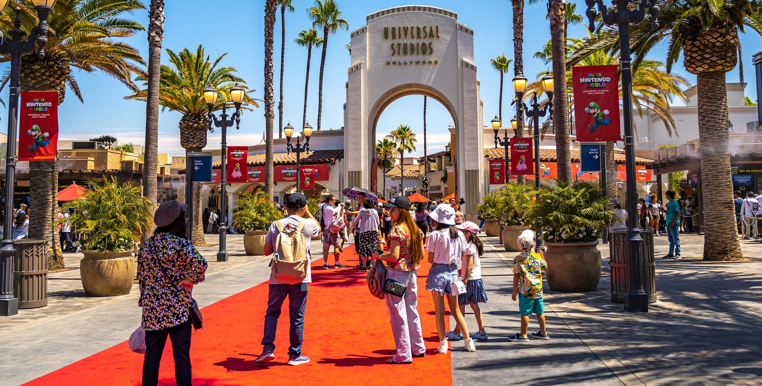 people walk towards Universal Studios Hollywood on a red carpet surrounded by palm trees