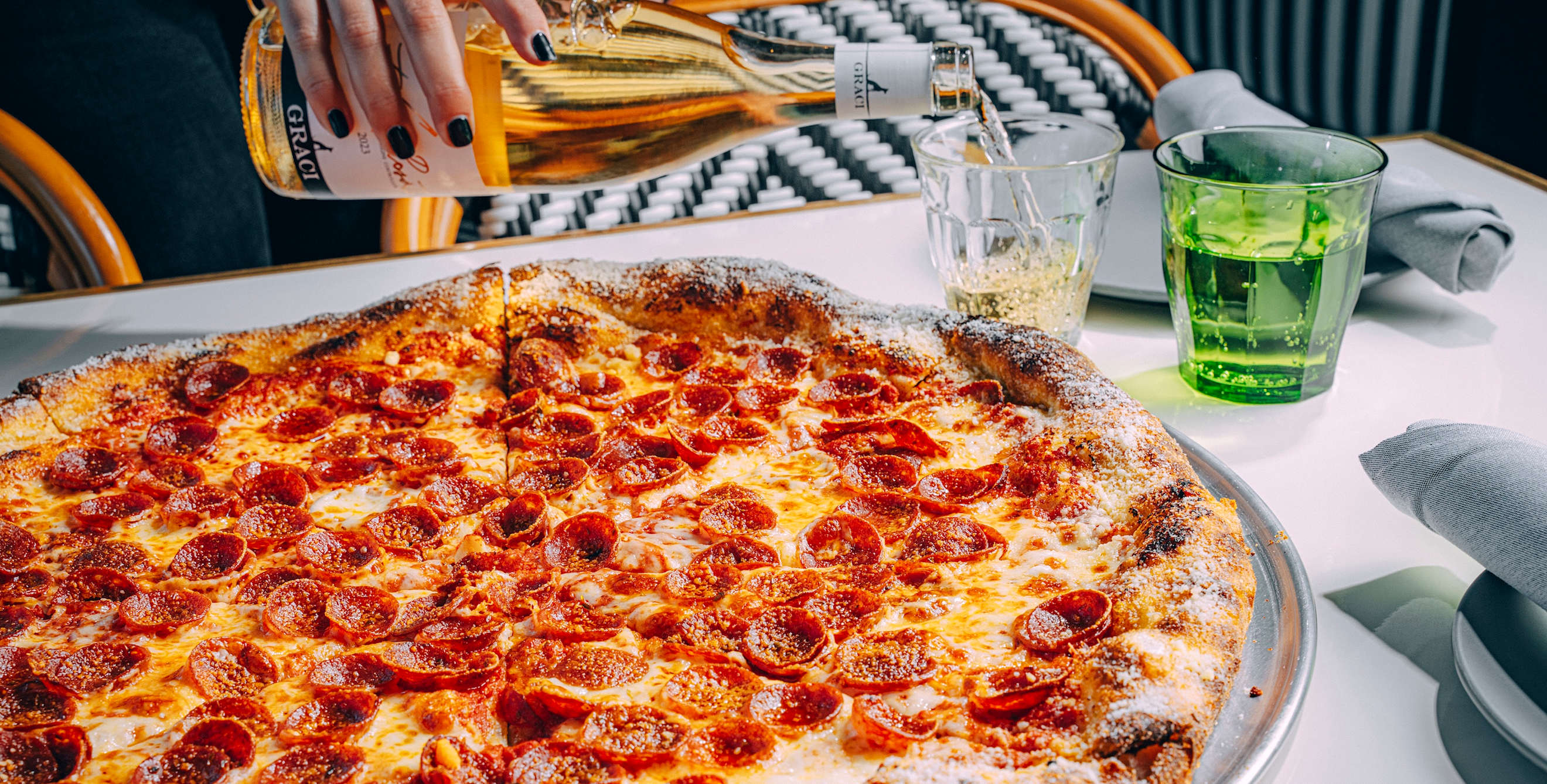 a large pepperoni pizza on a table with someone pouring wine