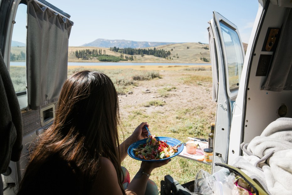 Picture of a woman eating lunch in a camper van looking towards mountains, picture