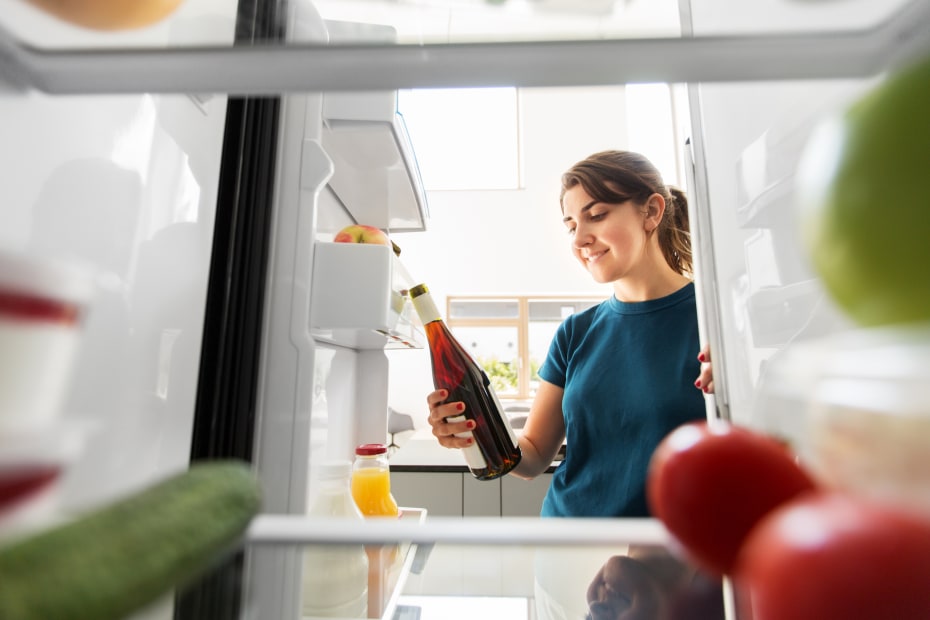 A woman removes a bottle of wine from her refrigerator.