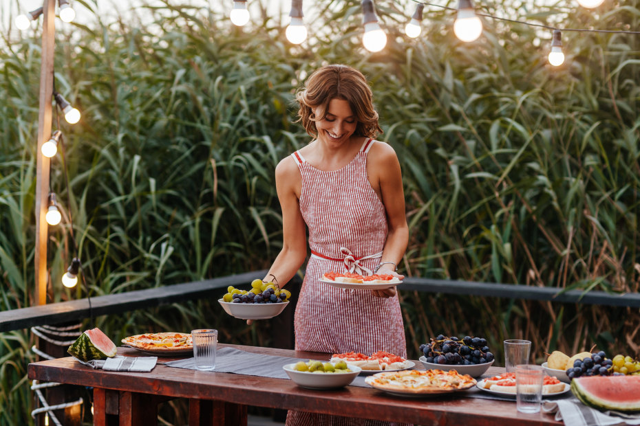 woman sets outdoor potluck barbecue table under string lights, image