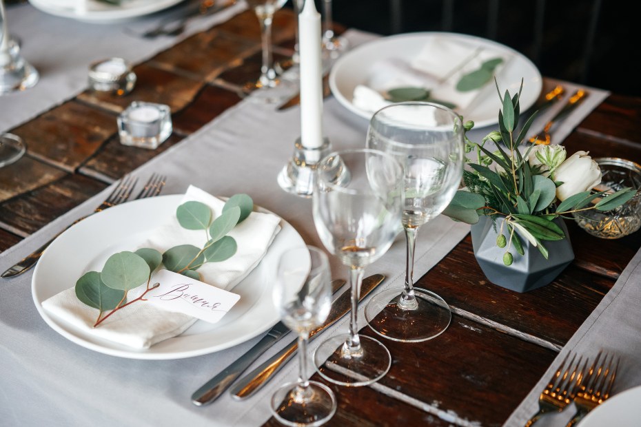 Eucalyptus leaves decorate a modern white Thanksgiving table and hold place cards, image