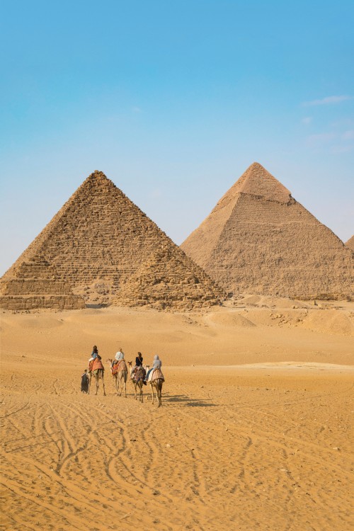 Tourists riding camels in front of the pyramids at Giza in Egypt, image