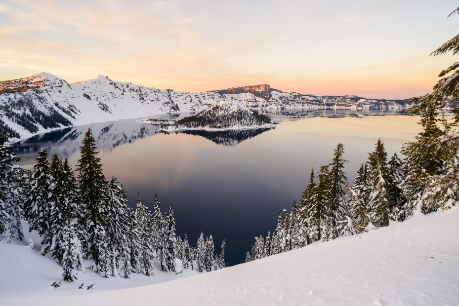 The sun turns the sky, snow, and lake yellow as it sets behind Crater Lake in Crater Lake National Park near Ashland, Oregon, picture