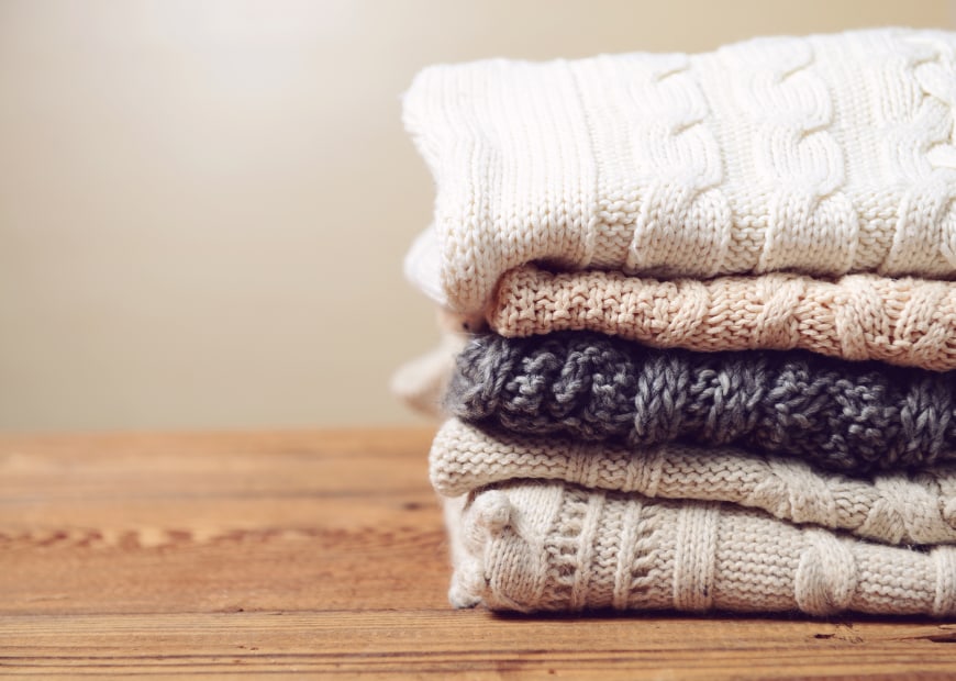 A stack of winter sweaters on a wood table, image