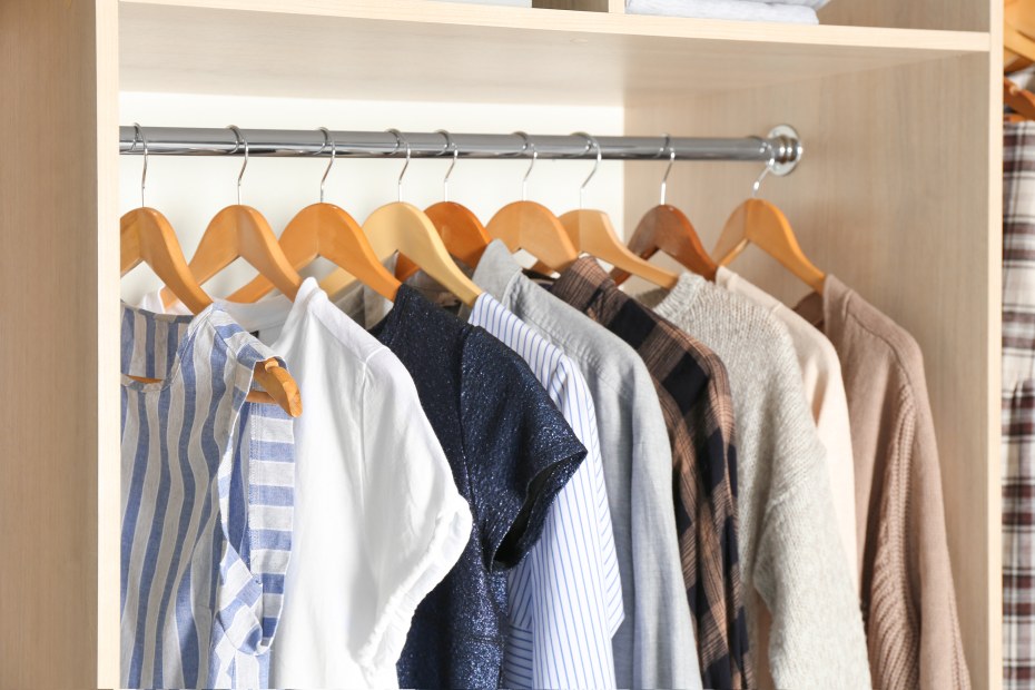 Modern minimalist women's clothing hangs on wooden hangers in a neat, organized closet, image