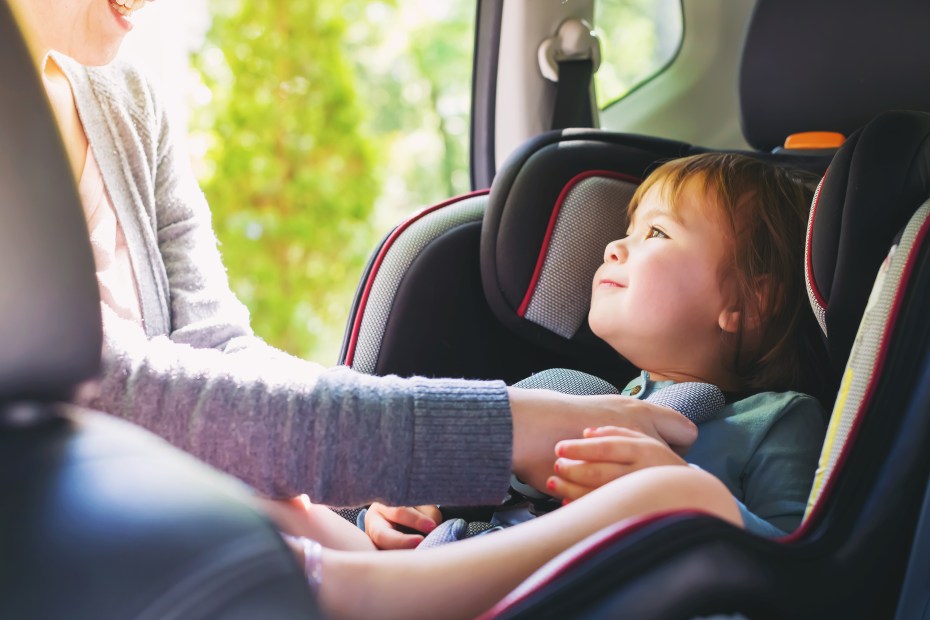 Mom buckles baby into car seat in the back of an SUV, image