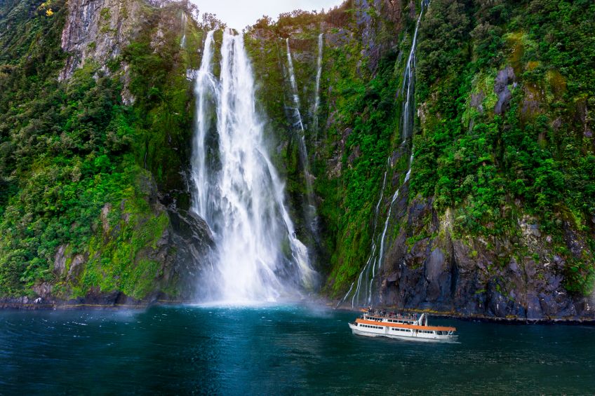 Tourist ferry carrying people approaching Stirling Falls at Milford Sound in South Island of New Zealand, image