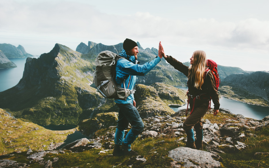 Picture of a couple sharing a high five while hiking on a lush green mountain in Norway, image