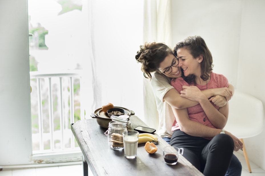 A lesbian couple embrace over breakfast, image