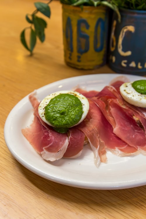 picture of a plate of poached eggs with arugula-herb purée and prosciutto at Carmel Belle in Carmel, California.