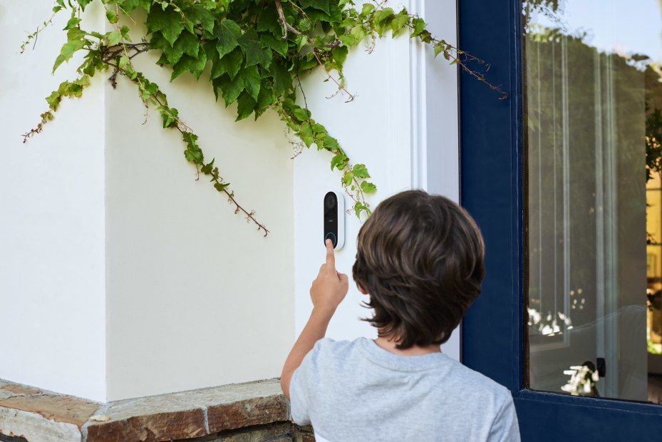 boy rings nest hello smart doorbell on the front of a modern house with a glass front door, image